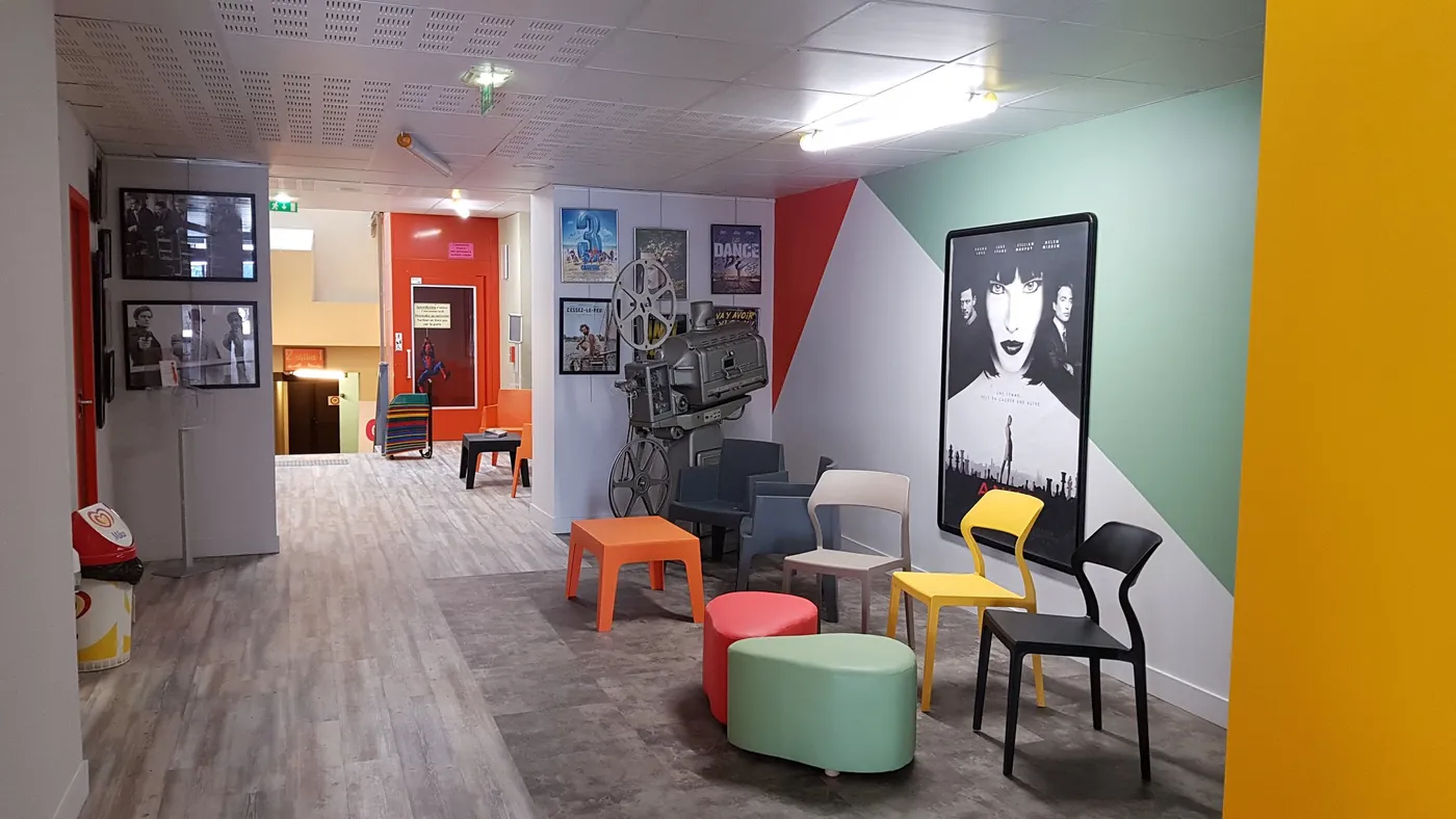Le hall du cinéma Le Palace : affiches encadrées, vieux projecteur, sièges et tables basses colorées